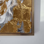 Close-up of a framed abstract wall art piece with textured gold, white, and gray brushstrokes, shown against a light gray wall.